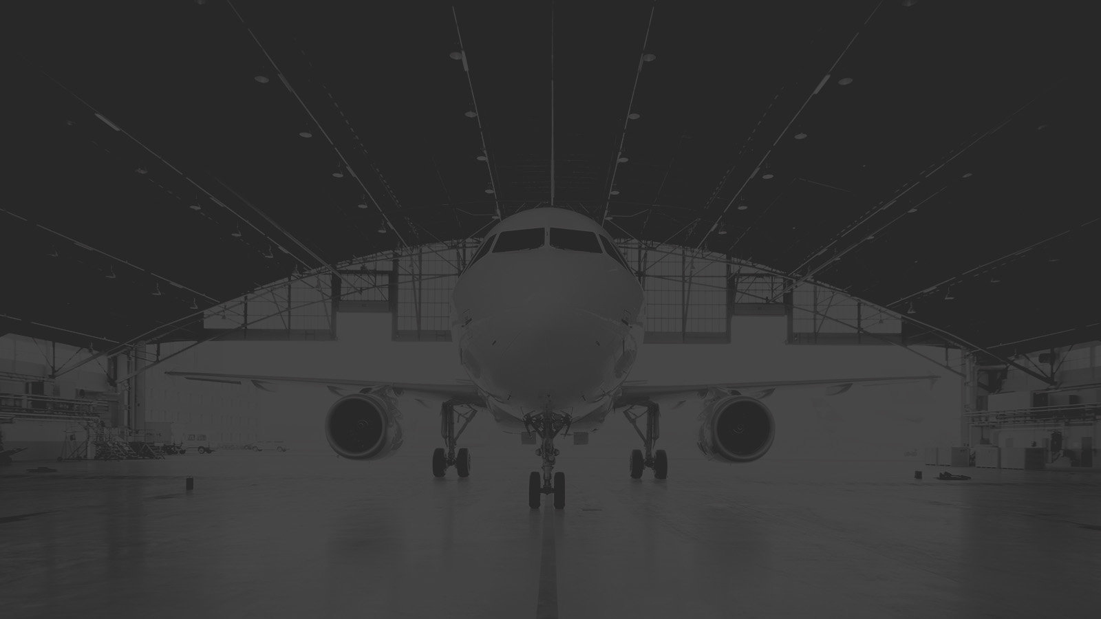 Front view of an airplane inside a large aircraft hangar with dramatic dark lighting.